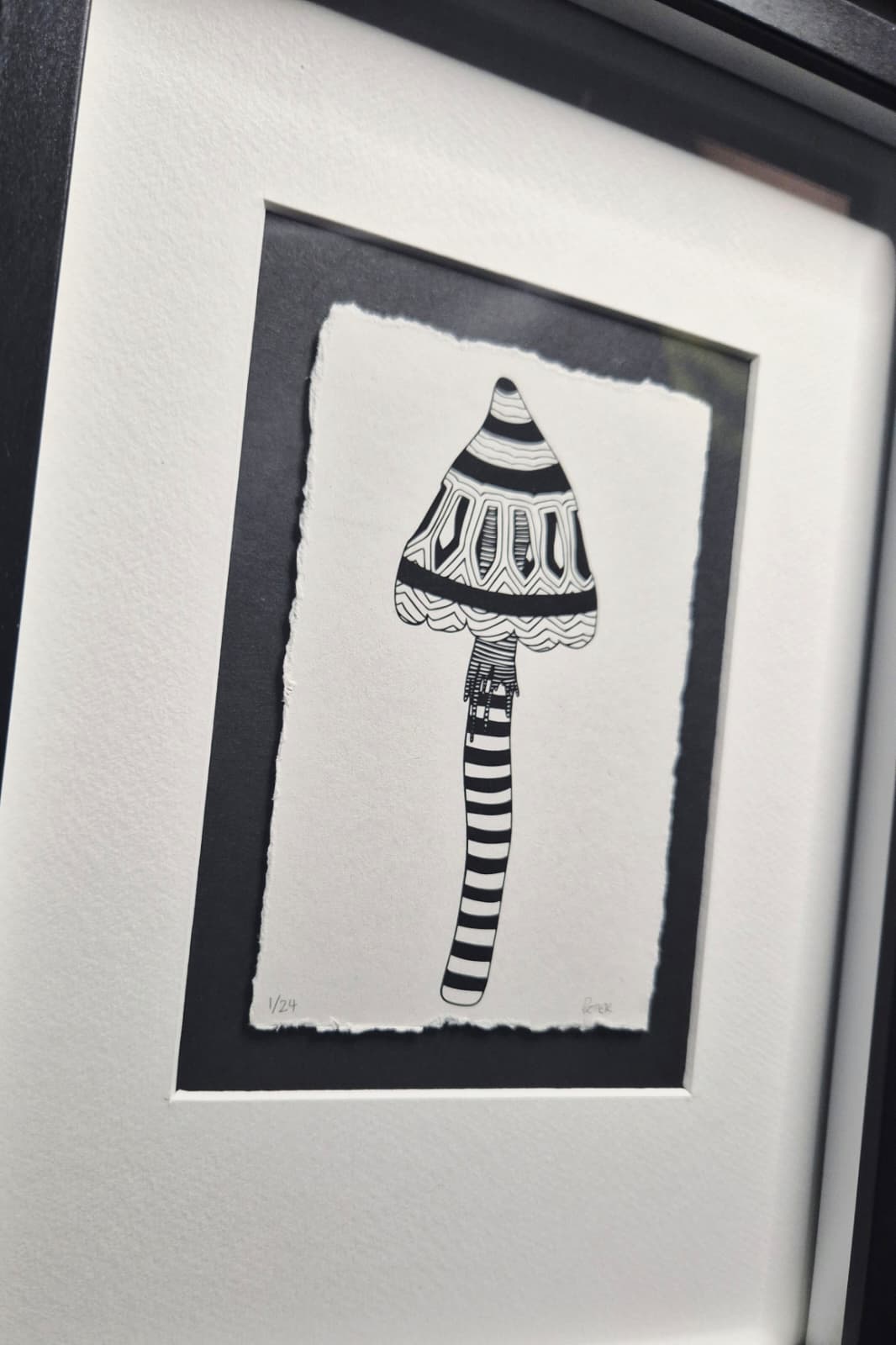 Framed black and white illustration of a striped mushroom on a textured recycled paper with black and white mount and black frame.